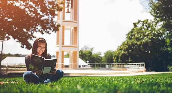 Student reading book on bell tower quad